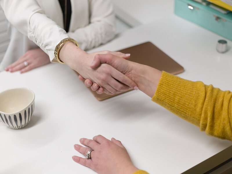 Two people shaking hands across a desk at the end of a conversation